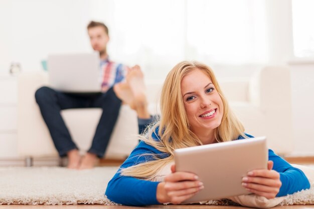 Schöne blonde Frau, die digitales Tablett verwendet und auf capet zu Hause entspannt