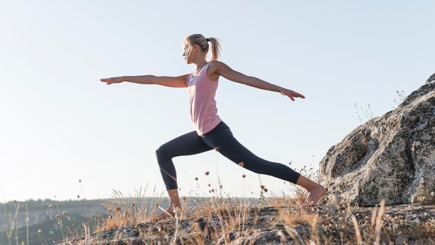 Schöne blonde Frau, die Yoga im Freien praktiziert