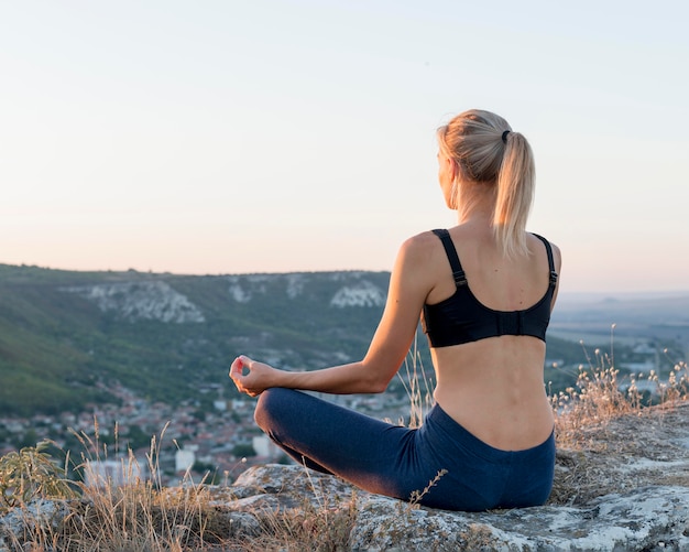 Schöne blonde Frau, die Yoga im Freien praktiziert