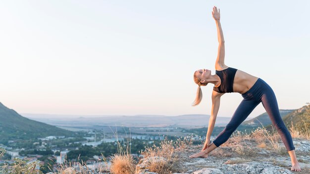 Schöne blonde Frau, die Yoga im Freien praktiziert