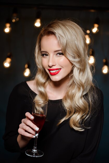 Schöne blonde Frau im Abendkleid lächelnd, Weinglas haltend