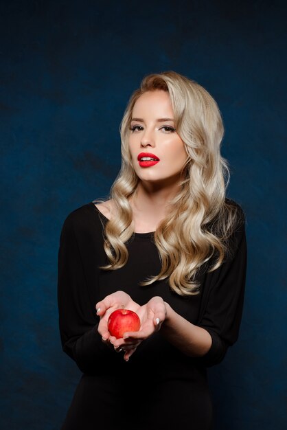 Schöne blonde Frau im schwarzen Kleid, das Apfel hält