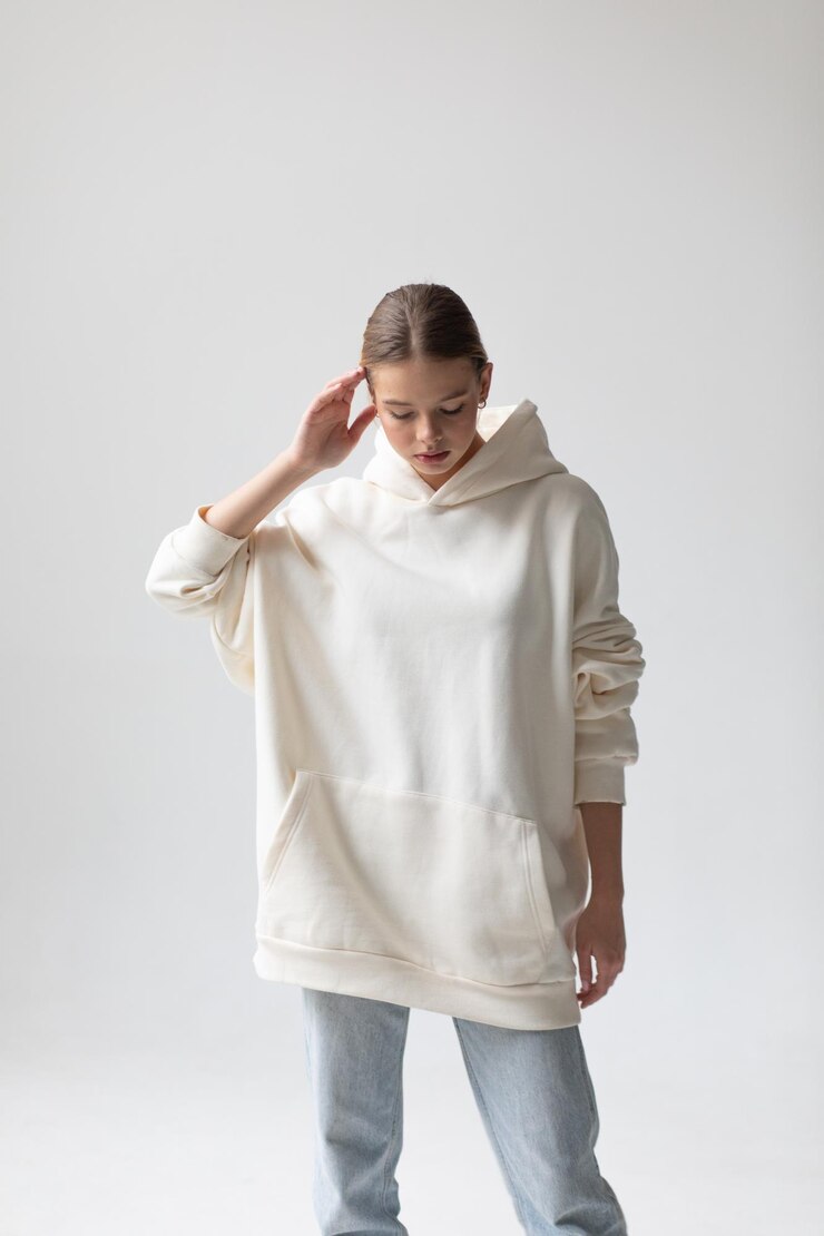 Schöne blonde Frau in einem weißen Hoodie und blauen Jeans posiert auf einem weißen Hintergrund