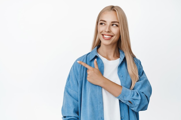 Schöne blonde Frau lächelt, zeigt mit dem Finger und blickt nach links auf das Firmenlogo, das Werbung zeigt, die über weißem Hintergrund steht