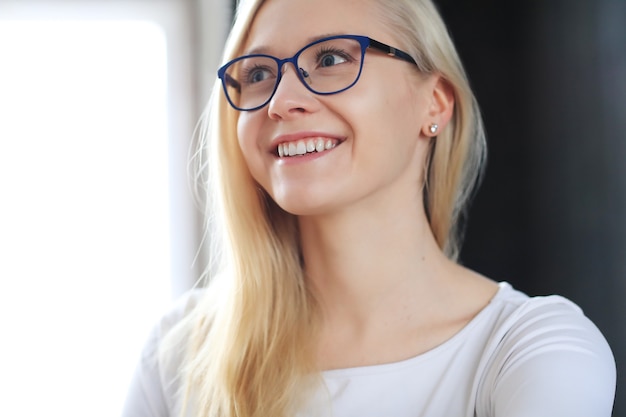 Schöne blonde Frau mit Brille, die im weißen Hemd aufwirft