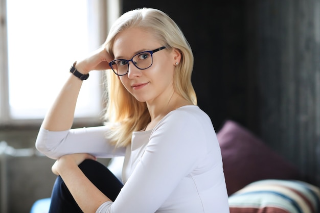 Schöne blonde Frau mit Brille, die im weißen Hemd aufwirft