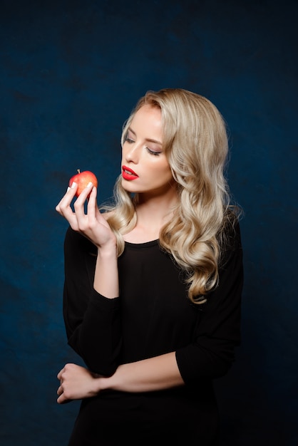 Schöne blonde Frau mit hellem Make-up im schwarzen Kleid, das Apfel hält