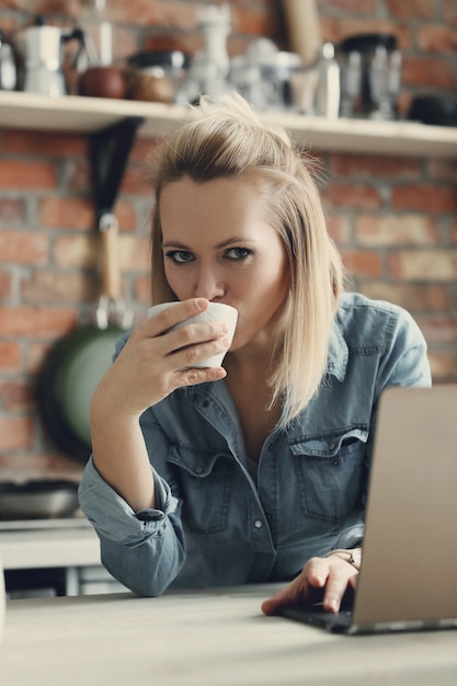 Schöne blonde Frau mit Kaffeetasse und Laptop