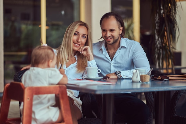 Schöne blonde Frau und hübscher Mann während der Zeit mit ihrer kleinen Tochter in einem Café im Freien. Familien- und Personenkonzept.