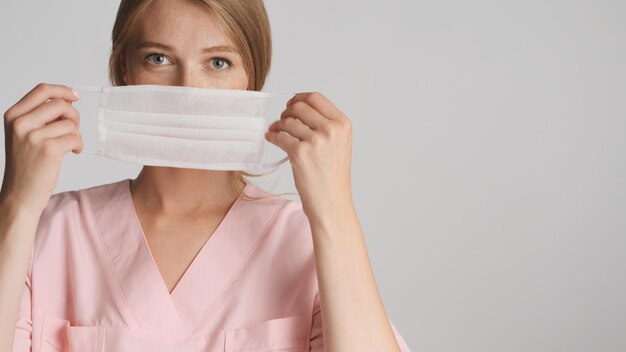 Schöne blonde Krankenschwester mit medizinischer Maske vor der Kamera mit Platz für Werbung oder Werbetext in der Nähe von weißem Hintergrund
