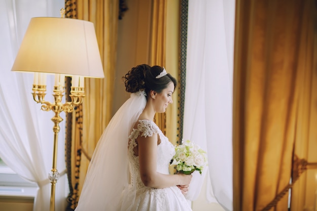 schöne Braut in einem weißen Kleid und eine Krone auf dem Kopf und einen Blumenstrauß