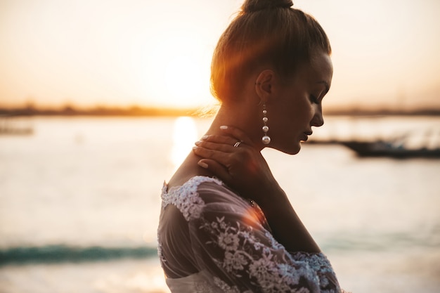 Schöne braut posiert am strand hinter dem meer bei sonnenuntergang