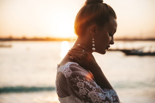 schöne Braut posiert am Strand hinter dem Meer bei Sonnenuntergang