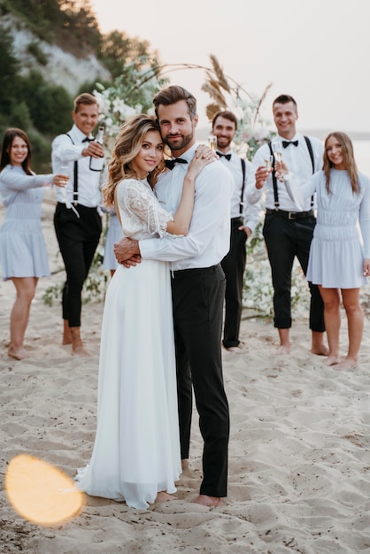 Schöne Braut und Bräutigam, die ihre Hochzeit mit Gästen am Strand haben