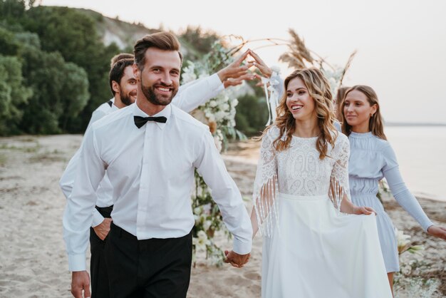 Schöne Braut und Bräutigam, die ihre Hochzeit mit Gästen am Strand haben