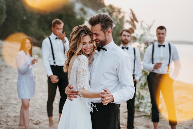Schöne Braut und Bräutigam haben ihre Hochzeit mit Gästen am Strand