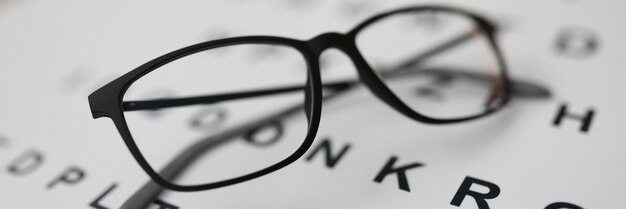 Schöne brille für das sehen liegt auf dem alphabet moderne schwarze umrandete brille bei einem sehtest