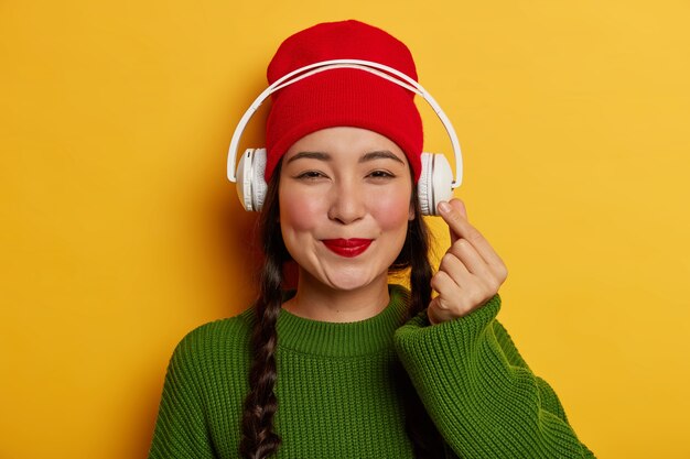 Schöne brünette Frau in rotem Hut und grünem Pullover, hört Audiospur