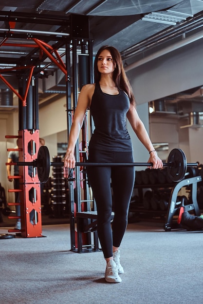 Schöne brünette Frau in Sportbekleidung hält beim Training im Fitnessclub oder Fitnessstudio eine Langhantel.