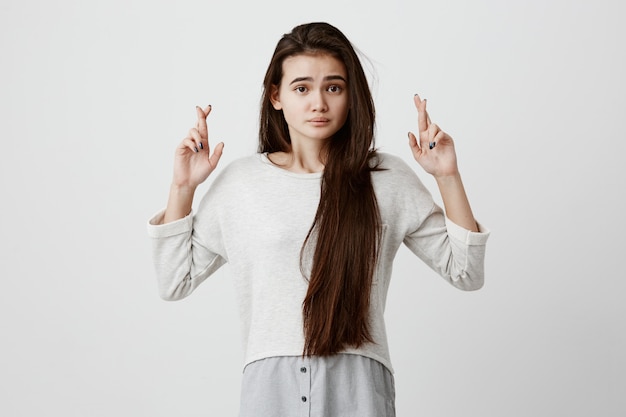 schöne brünette Frau mit langen Haaren, die aufgeregten, abergläubischen und naiven Blick hat, die Daumen drückt und auf viel Glück hofft, bevor sie die Prüfung besteht. Körpersprache und Gesten.