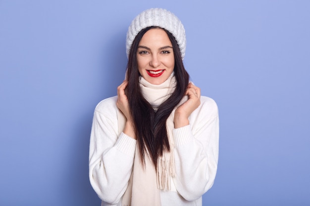 Schöne brünette Frau mit langen Haaren, die stilvolle warme Mütze und weißen Pullover tragen