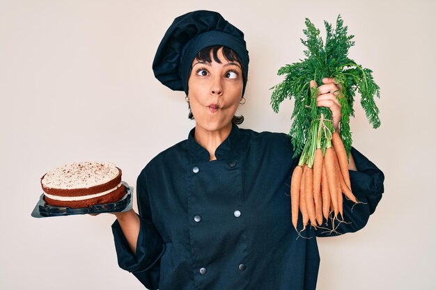 Kostenloses Foto schöne brünette köchin kocht karottenkuchen und macht ein fischgesicht mit mund und schielenden augen, verrückt und komisch.