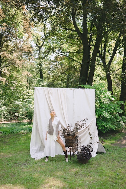 Schöne Dame, die nahe an den Blumen im weißen und grauen Kleid im Garten mit weißer Wand während des Tages steht.