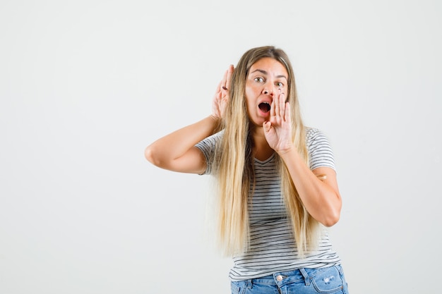 Schöne Dame, die schreit, während das Stimmenecho im T-Shirt hört und fokussierte Vorderansicht schaut.