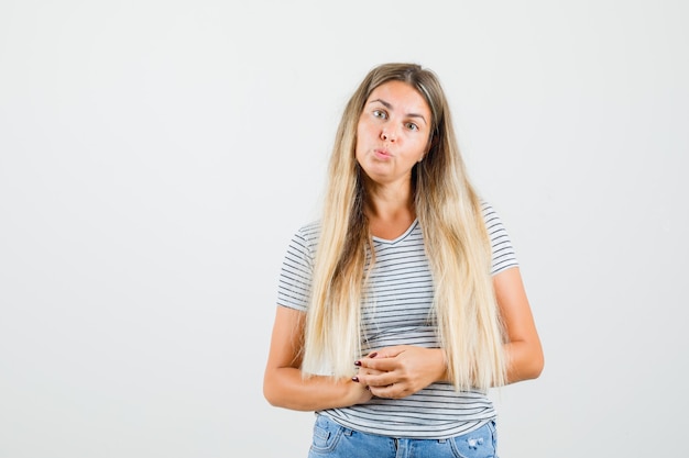 Schöne Dame im T-Shirt stehend, während sie ihre Lippen schmollt und ruhig schaut, Vorderansicht.