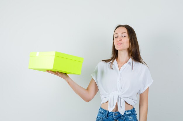 Schöne Dame in der weißen Bluse, Jeans, die Box hält und zufrieden schaut, Vorderansicht.