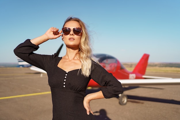 Schöne Dame mit Sonnenbrille posiert in der Nähe des Flugzeugs