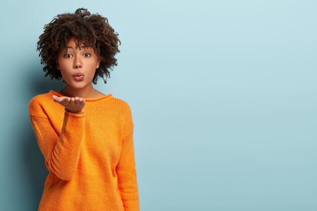 Schöne dunkelhäutige Frau mit Afro-Haaren schickt dem geliebten Freund einen Luftkuss, faltet die Lippen, die Handfläche ausgestreckt