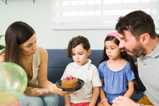 Schöne Eltern, die einen Kuchen zum Geburtstag ihres Sohnes bringen. Entzückender kleiner Junge, der eine Geburtstagskerze auf einem köstlichen Schokoladenkuchen durchbrennt