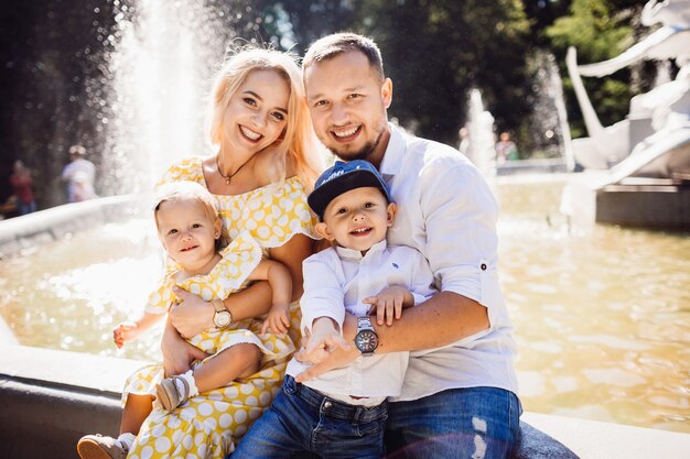 Schöne Familie in der gleichen Kleidung sitzt auf dem Brunnen mit ihren Kindern und gelben Ballons
