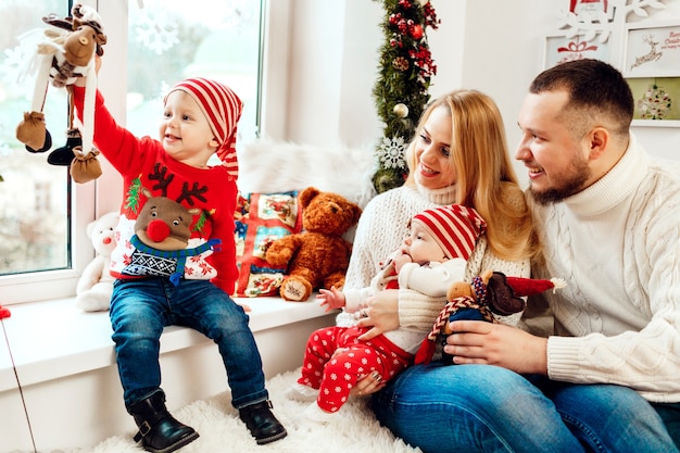 Schöne Familie mit Kindern in warmen Strickjacken wirft vor einer grünen Wand und einem reichen Weihnachtsbaum auf