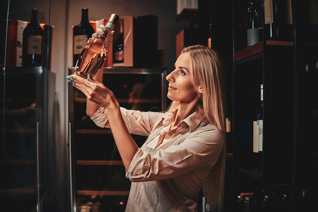 Kostenloses Foto schöne fokussierte frau wählt den richtigen wein für kunden im dunklen weinkeller aus.