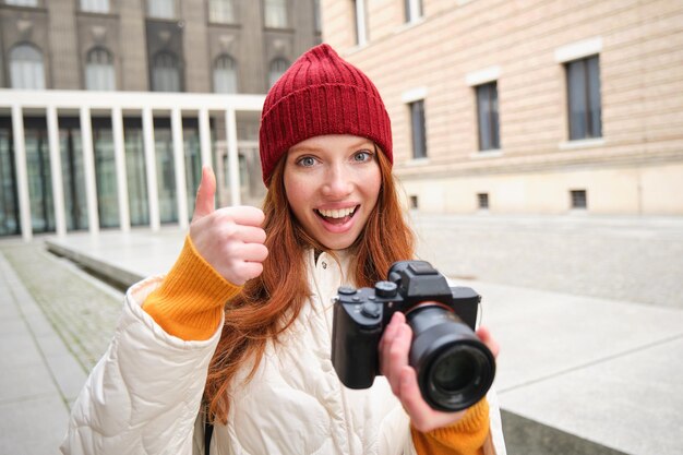 Schöne Fotografin mit Lesekopf und professioneller Kamera macht Fotos im Freien, die herumlaufen