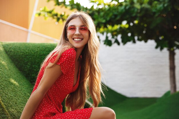 Schöne Frau, die auf Gras ruht und lächelt und tropische Sommerferien mit Sonnenbrille und Kleid genießt