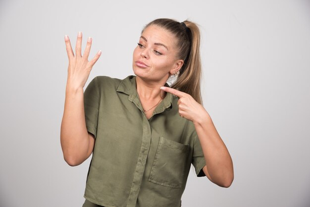 Schöne Frau, die auf ihre Hand auf grauer Wand zeigt