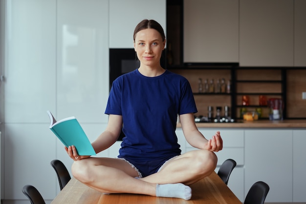 Schöne Frau, die auf Tisch in Yoga-Posen liest