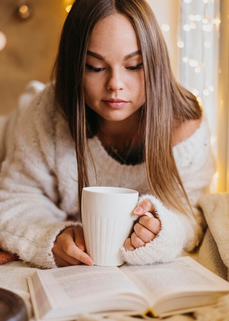 Schöne Frau, die ein Buch liest, während eine Tasse Tee hält