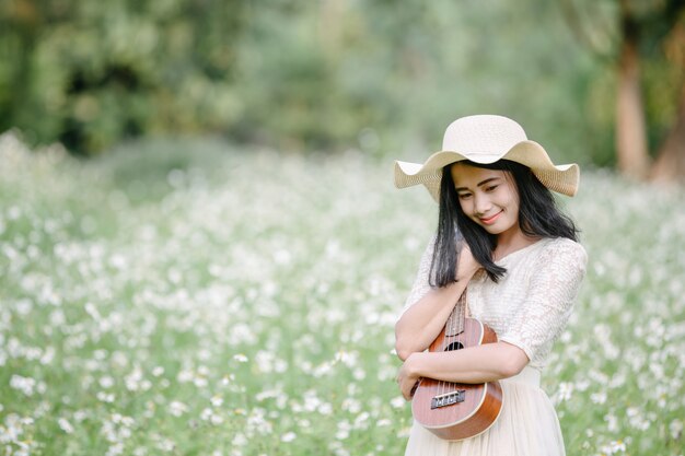 Schöne Frau, die ein nettes weißes Kleid trägt und eine Ukulele anhält