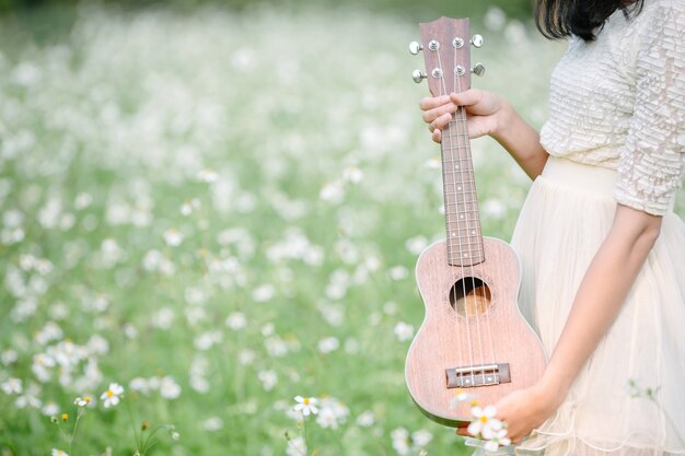 Schöne Frau, die ein nettes weißes Kleid trägt und eine Ukulele anhält