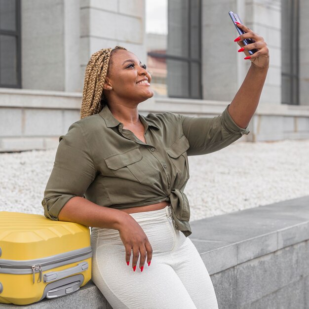 Schöne Frau, die ein Selfie neben ihrem gelben Gepäck nimmt