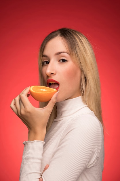 Schöne Frau, die eine Orange beißt