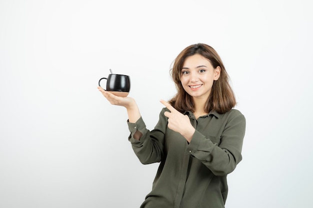 Schöne Frau, die eine Tasse Kaffee hält und darauf zeigt. Foto in hoher Qualität
