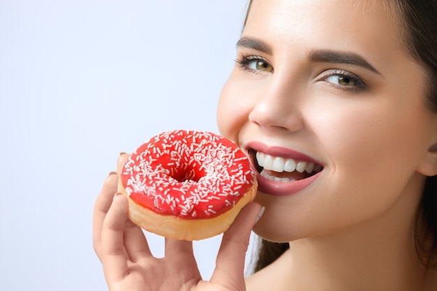 schöne Frau, die einen Donut am grauen Hintergrund beißt