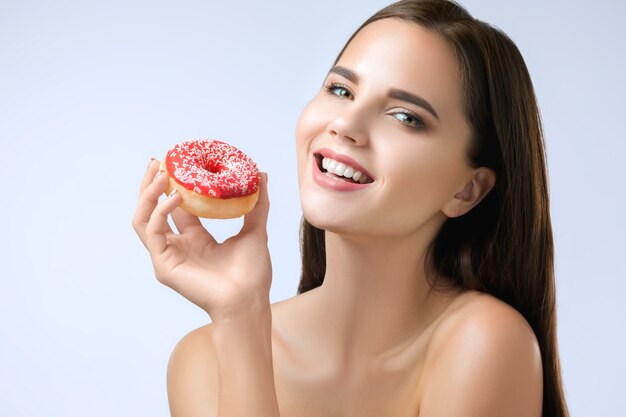 schöne Frau, die einen Donut am grauen Studiohintergrund beißt