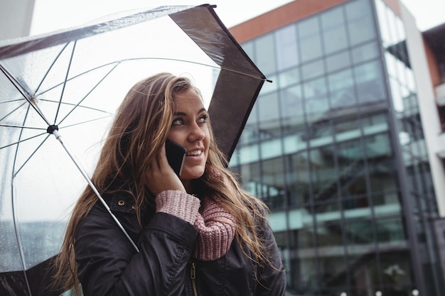 Schöne frau, die einen regenschirm anhält und am handy spricht