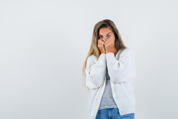 Schöne Frau, die Fäuste auf Gesicht in Jacke, T-Shirt hält und überwältigt, Vorderansicht schaut.